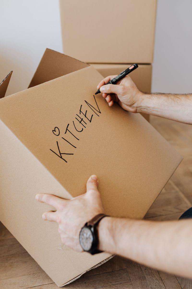 Person writing a label on a packed cardboard box with a marker